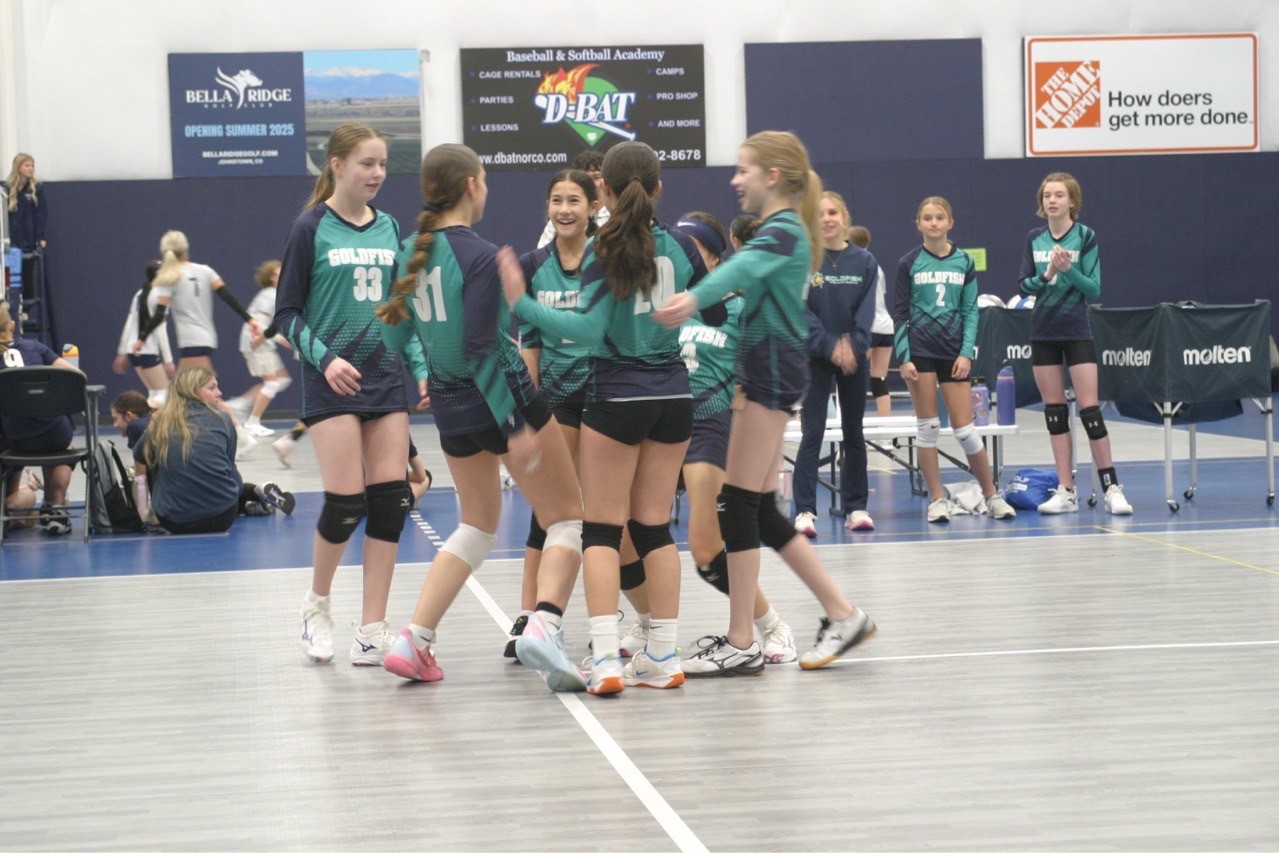 Huddle of teen volleyball players celebrating on court.